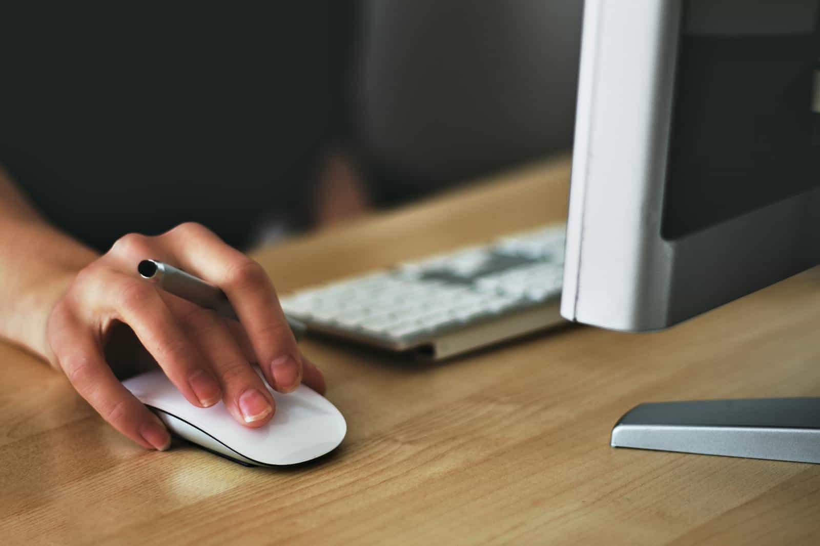 Lazy Loading. A hand using a wireless mouse at a modern desk setup with a computer and keyboard.