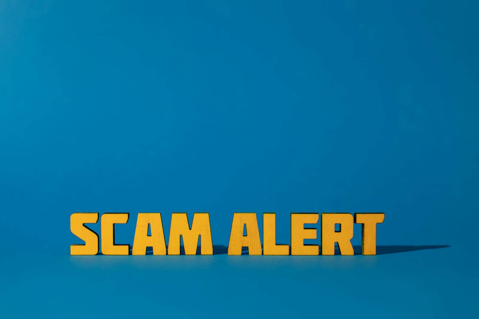 Bold yellow 'Scam Alert' text on a vivid blue surface, emphasizing warning and caution. Phishing scam