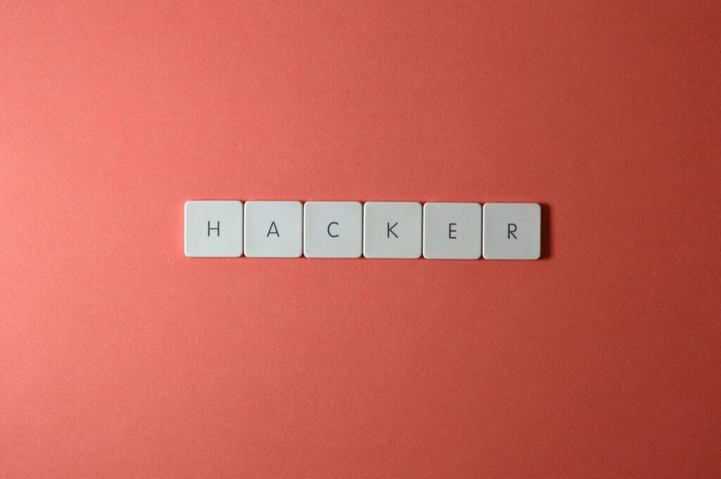 Password Management, Close-up of the word 'HACKER' made with letter tiles on a red background, emphasizing cybersecurity.