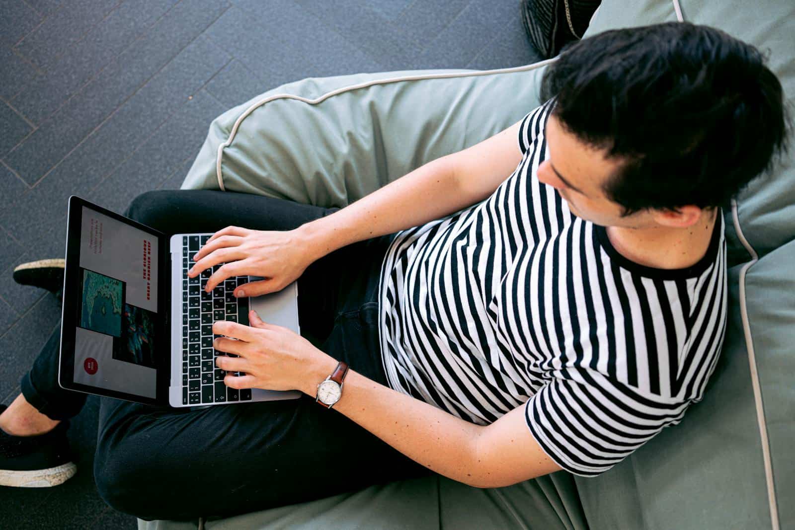 Online marketing, blogging, A man in a striped shirt using a laptop on a bean bag, embodying relaxed productivity.