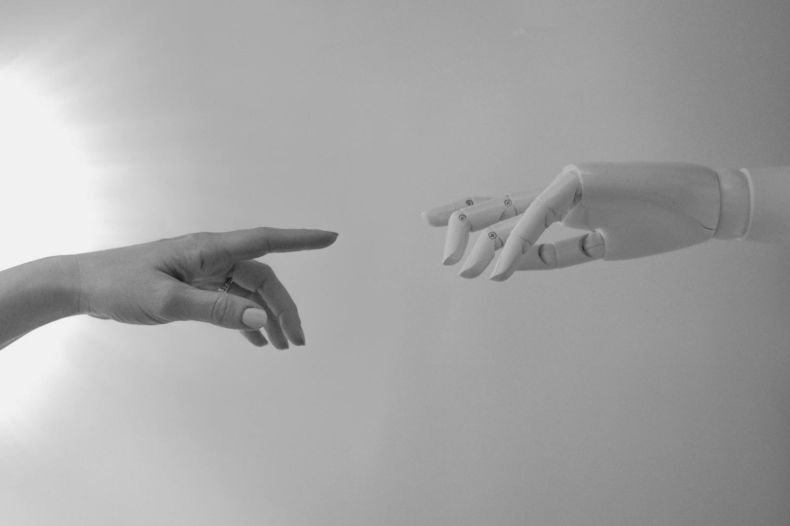 Neural Networks. Black and white image of a human and robotic hand reaching towards each other, symbolizing connection.