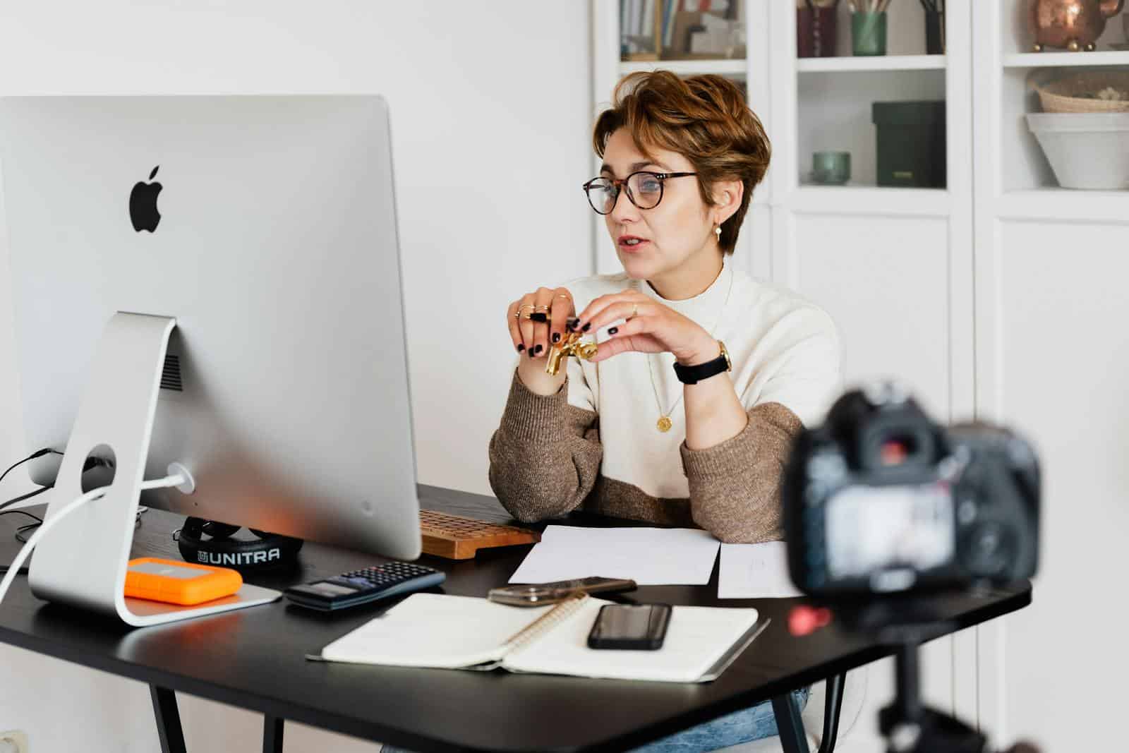 Hosting, Webinar, Engage, Educate, and Empower, A professional woman engaged in a virtual meeting setup at her home desk, using a computer and camera.