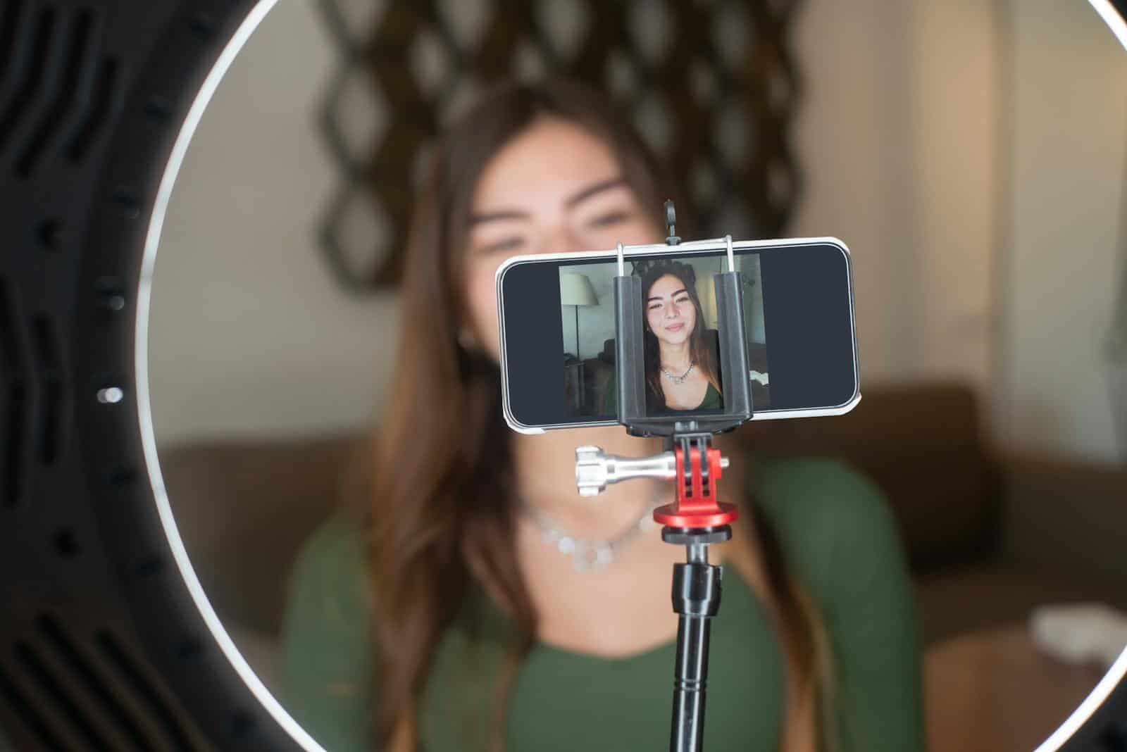 Live Streaming Video Marketing TrendsA young woman live streams from home using a smartphone and ring light setup.