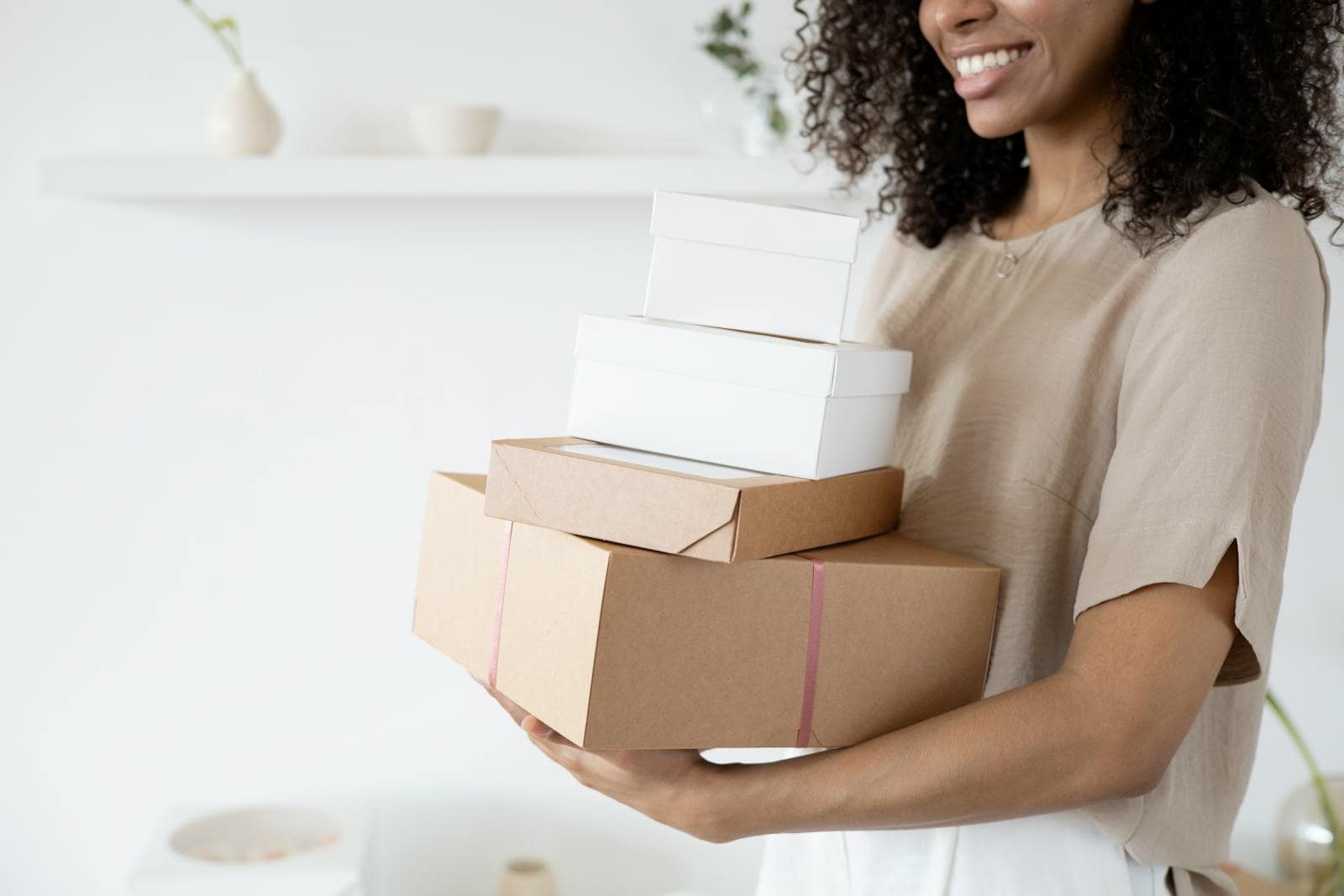 WooCommerce, online store, e-Commerce, Elementor, Woman with curly hair carrying stack of packaging boxes in a bright room.