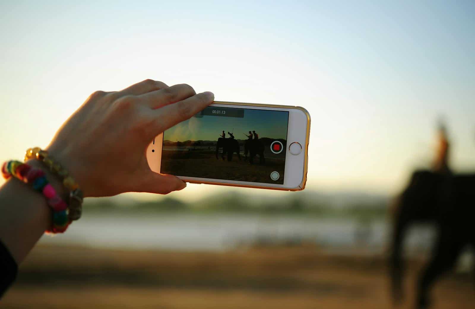 Video Marketing, A colorful bracelet-adorned hand holding a smartphone capturing elephants in the distance.