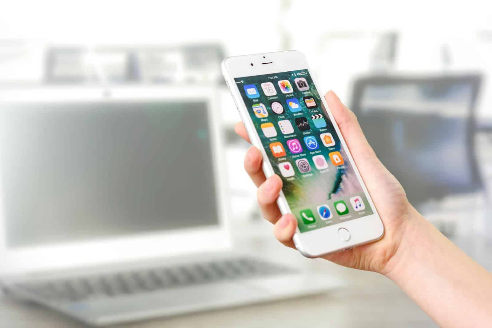 Content Generation, WP Autoblog, Content Generation, Content Promotion, Missinglettr, Publer, Newsletter, automation, promotion, Close-up view of a smartphone displaying apps, held by a hand, with a blurred laptop in the background.