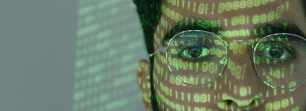 Close-up of a man with binary code projected on his face, symbolizing cybersecurity.