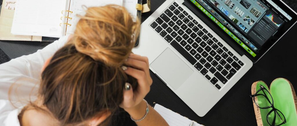 Overhead view of a stressed woman working at a desk with a laptop, phone, and notebooks.