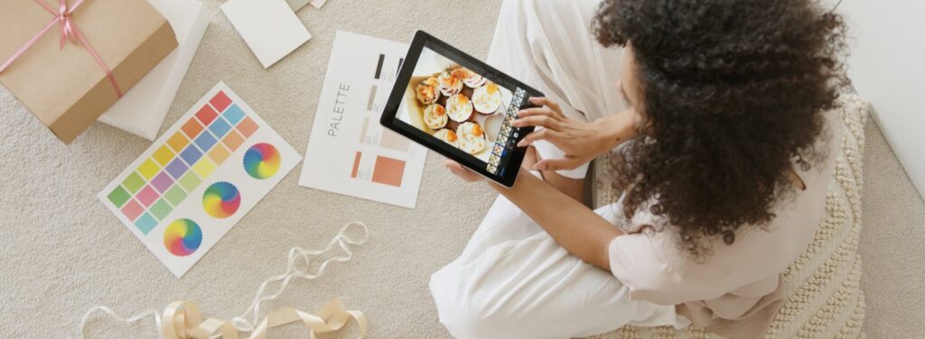Woman using tablet surrounded by design tools and gift box, showcasing creativity and online work.